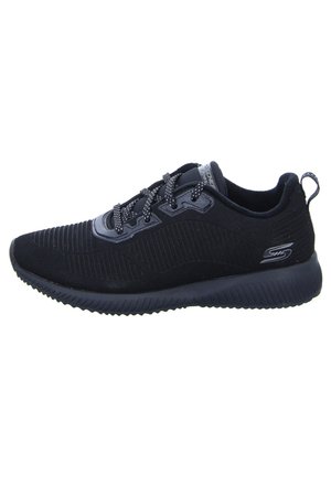 Zapatilla deportiva negra con una parte superior texturizada, diseño estriado y punta redonda. Cuerdas planas y suela acolchada. Logo de la marca en el lateral.