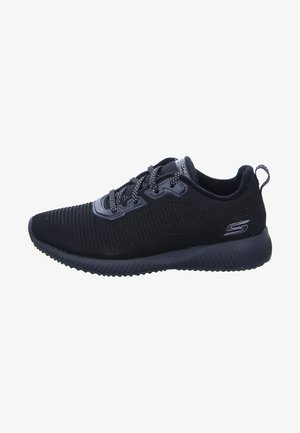 Zapatilla deportiva negra con una parte superior texturizada, diseño estriado y punta redonda. Cuerdas planas y suela acolchada. Logo de la marca en el lateral.