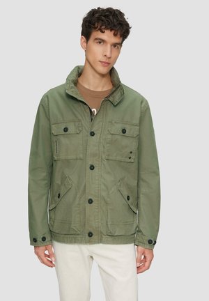 Veste légère vert olive avec col montant, fermeture à boutons, deux poches poitrine et deux poches latérales inférieures. Présente des boutons noirs.