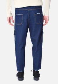 Pantaloni cargo in denim blu scuro con una vestibilità rilassata, dotati di molteplici tasche e orlo a maniche. Le tasche posteriori presentano decorazioni a contrasto.