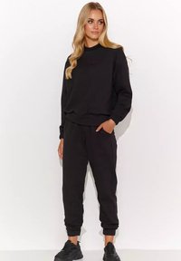 Czarna bluza i dresy w luźnym kroju, wykonane z miękkiej bawełny. Posiadają ściągacze przy mankietach, okrągły dekolt oraz boczne kieszenie.