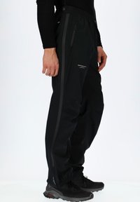 Svarta vattentäta byxor med en tapered passform, elastisk midja, sidofickor med dragkedja och reflexer för synlighet. Lättviktigt material.