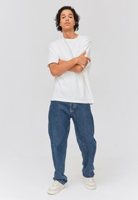 T-shirt blanc à manches courtes, coupe décontractée, associé à un jean en denim bleu ample. Baskets blanches avec des accents beiges. Design simple et épuré.