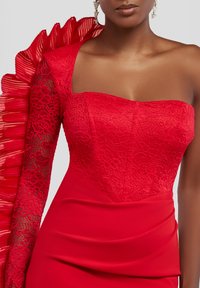 Rød kjole med en struktureret, blondeoverdel og en plisseret flæse på den ene skulder, med en draperet nederdel for en strømlinet silhuet.