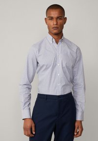 Witte blouse met een blauw en rood ruitpatroon, lange mouwen, en een klassieke kraag, gecombineerd met donkerblauwe broek.