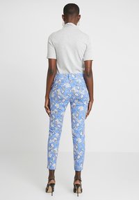 Blue patterned pants featuring floral designs, tailored fit, and a high waistband. Paired with a gray short-sleeve top and black heels.