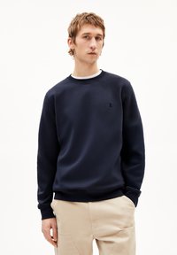 Marineblauwe sweatshirt met ronde hals, ribbels aan de mouwen en een klein geborduurd logo op de borst. Gemaakt van zachte, gestructureerde stof.