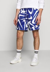 Blå mönstrade shorts med vita abstrakta mönster, med elastisk midja och dragsko. Matchas med vita sneakers och randiga strumpor.