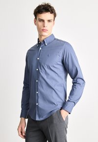 Modrá košeľa na gombíky z hladkej l�átky, s golierom, dlhými rukávmi a malým vyšívaným logom na hrudi.