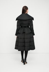 Black puffer coat with a structured oversized collar, cinched waist, and peplum hem, featuring quilted panels and a smooth texture.