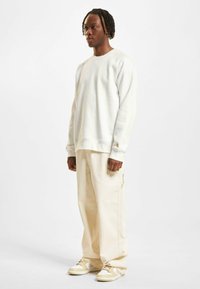 Weißer Sweatshirt mit lässiger Passform, kombiniert mit hellbeigen Cargo-Hosen und beigen Sneakers mit weißen Akzenten und strukturiertem Design.