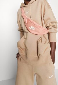 Rosa Nike midjeväska med ett dragkedjefack, justerbar rem och logotryck. Buren över en beige huvtröja och matchande sweatpants.