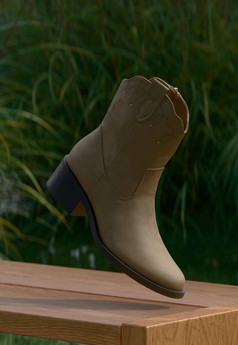 Μπότα αστραγάλου από ταμπά σουέντ με διακοσμητικό ράψιμο και χαμηλό χοντρό τακούνι, ακουμπισμένη στην άκ ρη μιας ξύλινης επιφάνειας έξω.