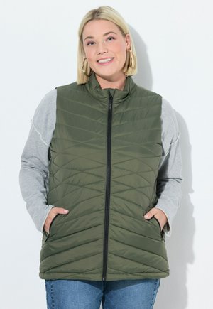 Chaleco acolchado verde oliva con cuello alto, cierre de cremallera y bolsillos frontales, combinado con una camiseta de manga larga gris.