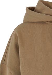 Sweat à capuche marron avec texture côtelée, manches larges et grande capuche. Le tissu est doux, offrant une coupe décontractée.