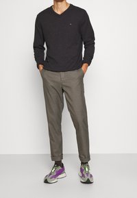 Maglietta a V grigia scuro a maniche lunghe, pantaloni a quadretti beige e neri, e sneaker multicolori con accenti viola e verdi.