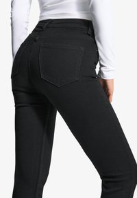 Svarta denimjeans med slim fit. Har två bakfickor med klassisk design, hög midja och en mjuk textur. Vit topp syns ovanför.