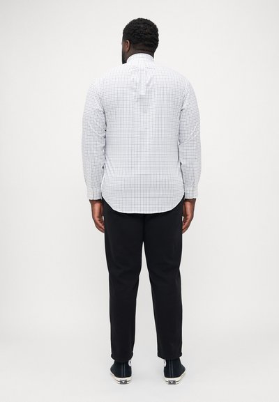 Chemise à manches longues à motif à carreaux en blanc et marine. Présente un pli au dos, un ourlet arrondi, et un pantalon noir avec des ourlets à revers.