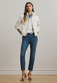 Balta denima jaka ar divām priekšējām kabatām, apvienota ar baltu kreklu ar zilu ziedu dizainu un vidēji izmaksātiem ziliem džinsiem. Brūnas kurpes ar siksniņām.