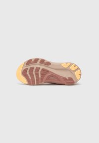 Schuhsohle mit einem beigen Gummibasis, strukturierten Oberfläche, lila Akzenten und gelben Traktionselementen in einem wellenförmigen Design.