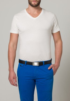 Weißes V-Ausschnitt-T-Shirt kombiniert mit leuchtend blauen Hosen, ergänzt durch einen schwarzen Gürtel mit einer silbernen Schnalle, dargestellt an einem Mann.
