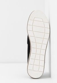 Chaussure en suede noire avec une semelle en caoutchouc blanche. La semelle présente un motif texturé pour une meilleure traction. Taille 37 indiquée sur le côté intérieur.