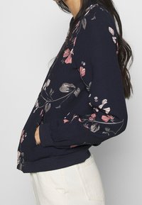 Donkerblauw sweatshirt met roze en grijze bloemenpatronen. Heeft een ronde halslijn, geribbelde manchetten en een losse pasvorm.