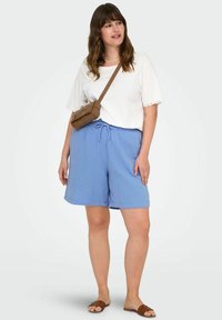 Světle modré šortky s páskem na stažení, spárované s bílým tričkem s krátkým rukávem a krajkovým lemem. Hnědá crossbody taška a ploché sandály.