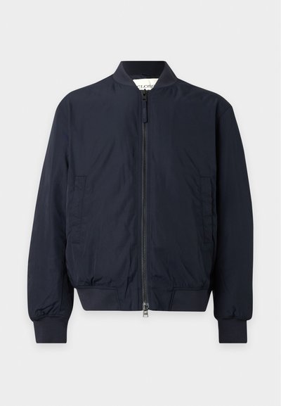 Blouson aviateur bleu marine avec fermeture éclair à l'avant, col, poignets et taille côtelés, et deux poches latérales sur un fond uni.
