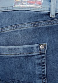 Modré džíny vyrobené z denimu s zadní kapsou a stříbrným knoflíkem a holografickou etiketou se nápisem "DENIM LOVE". Klasické detaily v šití.