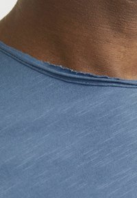 Blue cotton t-shirt with a close-up view of a slightly frayed neckline and textured fabric, showing fine horizontal stripes.