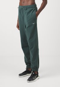Gröna fleece joggerbyxor med elastiska muddar, justerbart midjeband och sidofickor. Har en liten vit Nike-logga på höften.