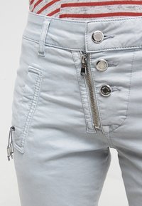 Ljusblå denimbyxor med dragkedja, knappstängning och sidoficka. Har strukturerad tyg och silverfärgade detaljer.