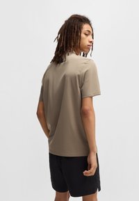 T-shirt beige con maniche corte, texture liscia e scollatura rotonda. Abbinato a pantaloni corti neri, visto da dietro su uno sfondo neutro.