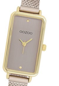 Montre rectangulaire dorée avec un cadran en métal gris brossé, au design minimaliste, et un bracelet en maille beige texturé. Présente un logo et des marqueurs d'heure simples.