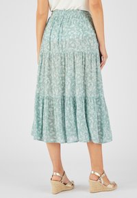 Jupe longue en teal clair avec des motifs floraux blancs. Fabriquée en tissu léger, elle présente une taille élastique et un ourlet à volants.