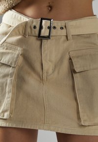 Khaki-Denim-Rock mit breitem Bund, Fronttaschen, einer großen silbernen Schnalle und sichtbaren Nähdetails.