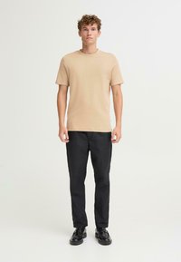 Beige cotton t-shirt with a crew neck, paired with black trousers and black shoes. Simple design, short sleeves, and a casual fit.
