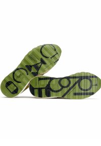 Suelas de zapatos de goma verde con surcos texturizados y grandes letras negras. Presentan un borde de color claro en contraste y detalles impresos.