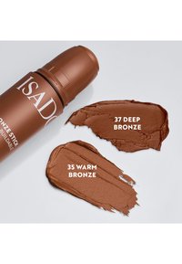 Tube de maquillage en stick bronze avec deux échantillons étiquetés 37 Deep Bronze et 35 Warm Bronze sur une surface claire.