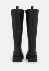 Schwarze kniehohe Stiefel aus glattem Material, mit einem groben Profil, vertikalen Nähten und Zugschlaufen an der Oberseite für einen einfachen Einstieg.