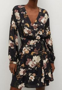 Vestido negro con estampado floral, de mangas largas y diseño cruzado, que presenta grandes flores blancas, rosas y naranjas, tejido texturizado y un lazo en la cintura.