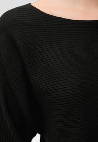 Schwarzer gerippter Strickstoff auf einem Kleidungsstück, das eine Nahaufnahme des Schulter- und oberen Brustbereichs zeigt.