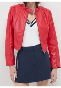 Rode jas van nep leer met een kort ontwerp, aansluitende stijl, kraag met drukknopen en ritssluiting aan de voorkant. Draagt over een wit topje en een marineblauwe rok.