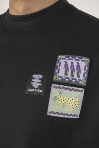 Czarny sweatshirt z trzema naszytymi łatami: logo węża, ptaki w purpurowej ramce oraz nakrapiany leopard na zielonym tle.