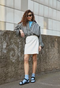 Pasiasta, oversize bluzka z podwiniętymi rękawami, biała mini spódnica oraz czarne sandały z niebieskimi skarpetkami. Casualowy strój z kontrastującymi fakturami.