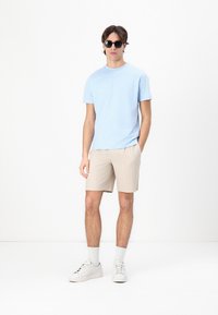 Lyseblå kortermet t-skjorte, beige stripete shorts, hvite joggesko og svarte solbriller. Glatt stoff, avslappet passform, uformell stil.
