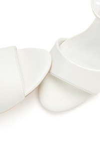 White sandals with a smooth leather exterior, open-toe design, wide strap across the foot, and a padded inner sole.