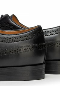 Czarne skórzane eleganckie buty z perforowanymi zdobieniami brogue, gładkim wykończeniem, zaokrąglonym noskiem i piętą na słupku. Wytrzymała skórzana podeszwa.