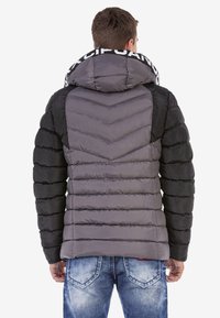 Chaqueta acolchada con un patrón de chevron en gris y negro, con una gran capucha y texto en contraste en el cuello. Tejido suave y aislante.